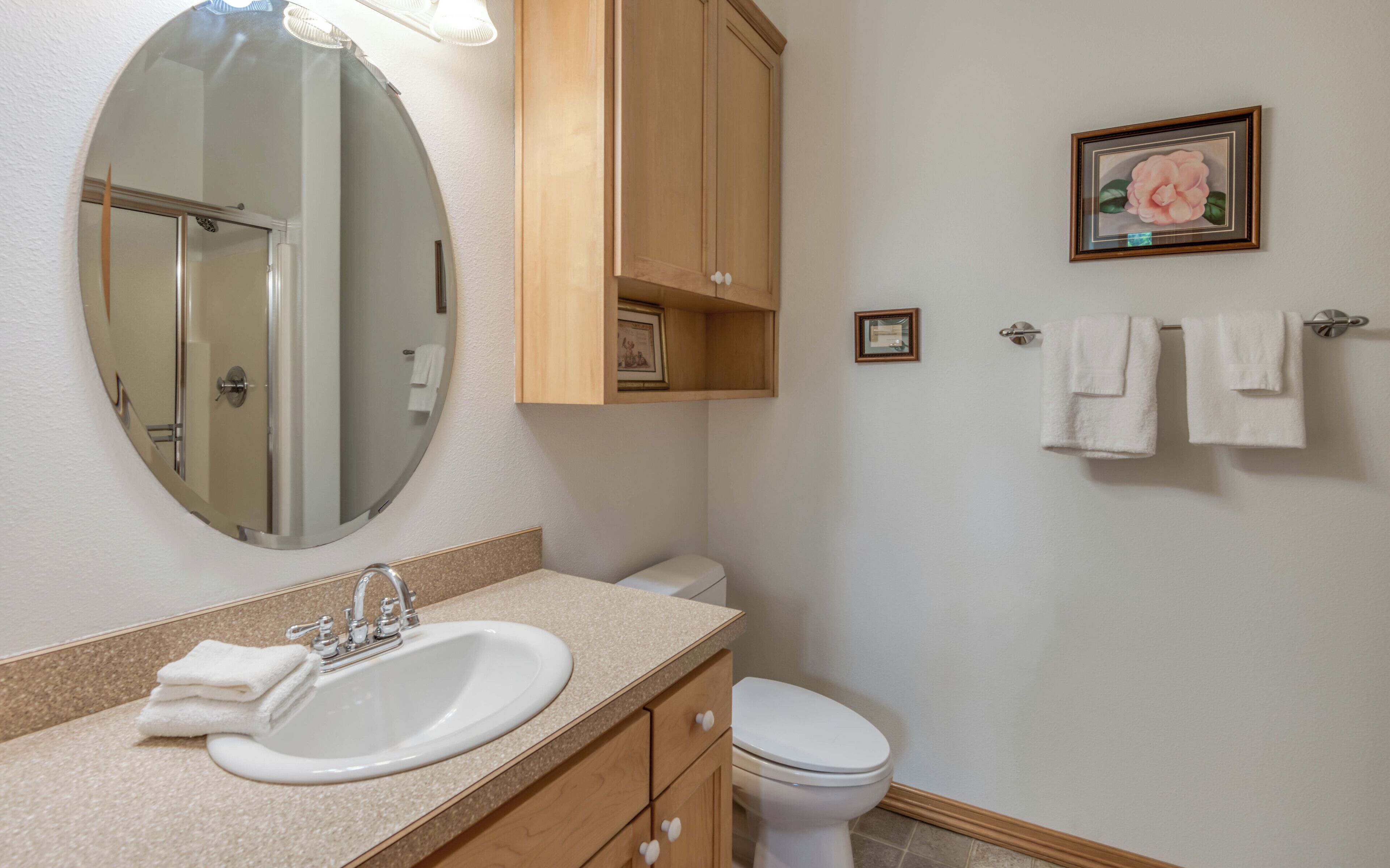 Une salle de bain avec un lavabo, un miroir, un meuble en bois, des toilettes et un tableau encadré au mur.