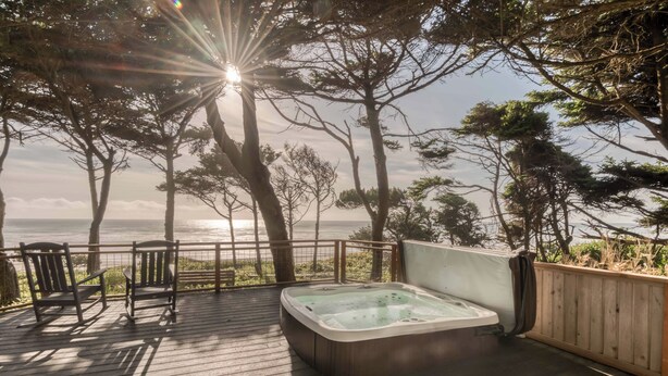 Una terraza de madera con un jacuzzi, sillas y vista al océano.