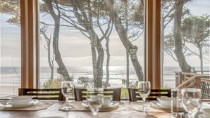 Mesa lista para comer con vista al océano y árboles a través de amplios ventanales.