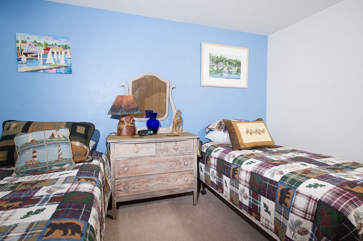 A bedroom with two beds, a dresser, a mirror, and two framed pictures on the wall.