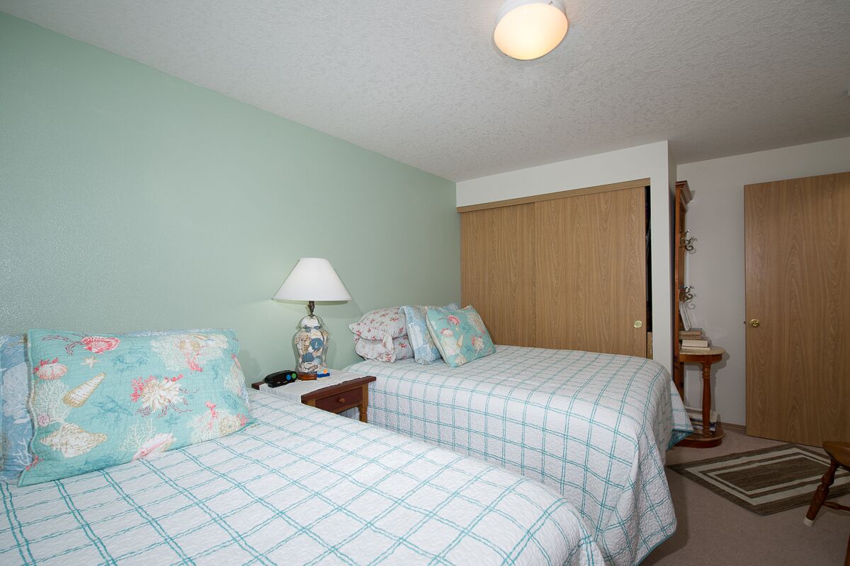 A bedroom with two beds, a nightstand, a lamp, and a wooden wardrobe.
