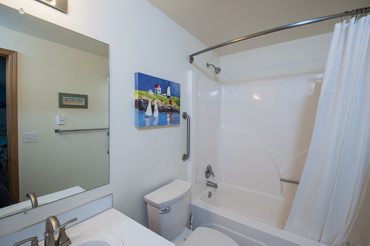 Un baño con lavamanos, inodoro y bañera blancos. En la pared, un cuadro con faros.