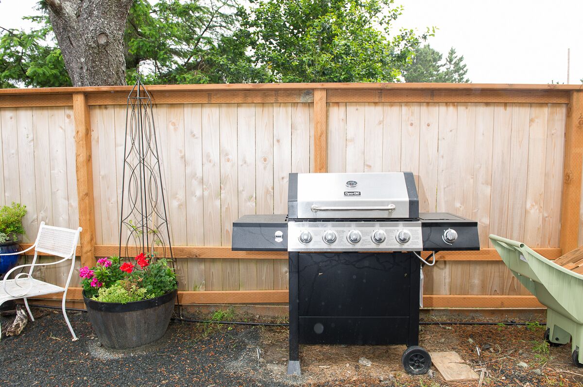 A backyard with a barbecue grill, a white chair, and a planter with flowers.