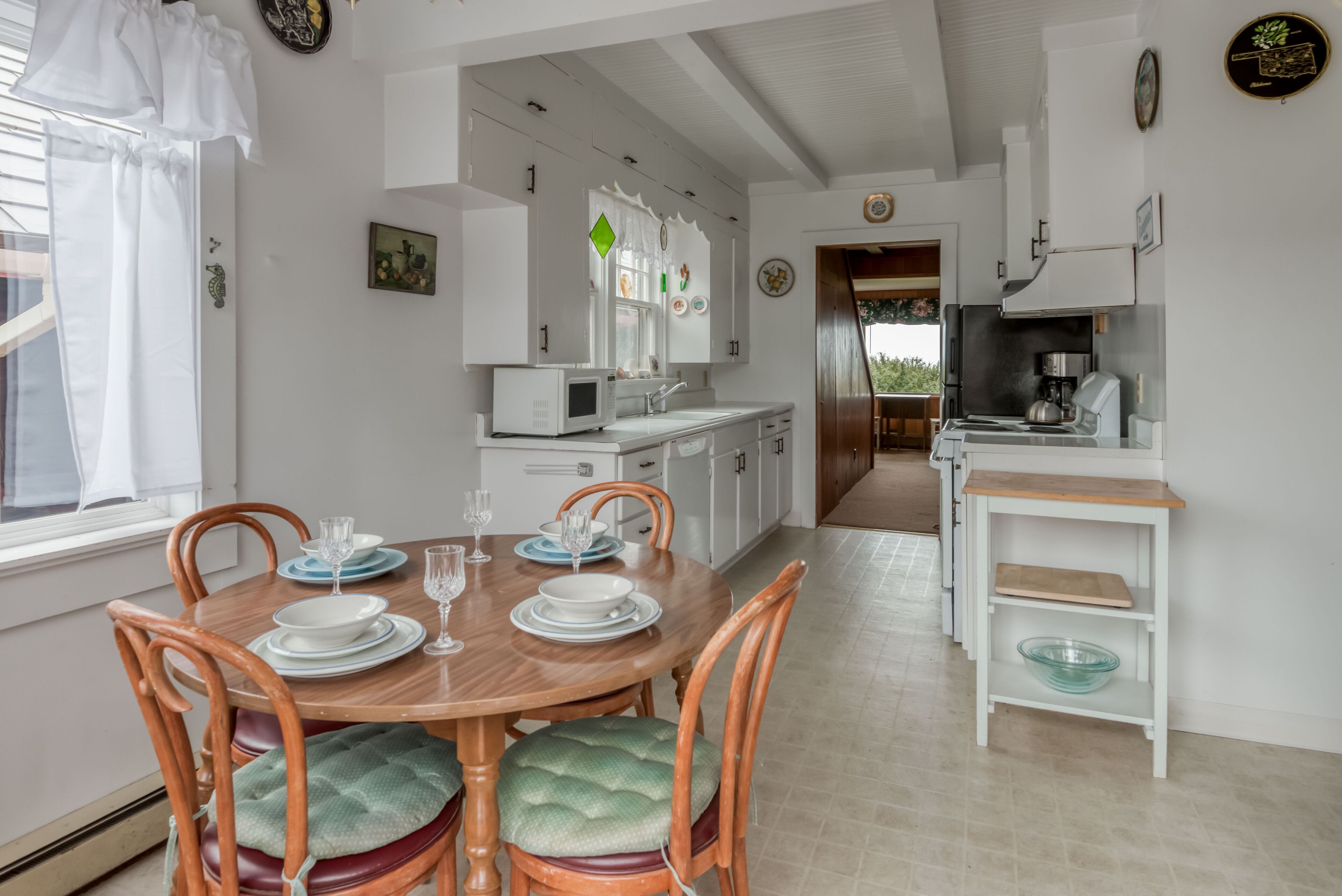 Un coin repas avec une table et des chaises en bois, une cuisine avec des meubles blancs et un four à micro-ondes, et une vue sur l’extérieur.