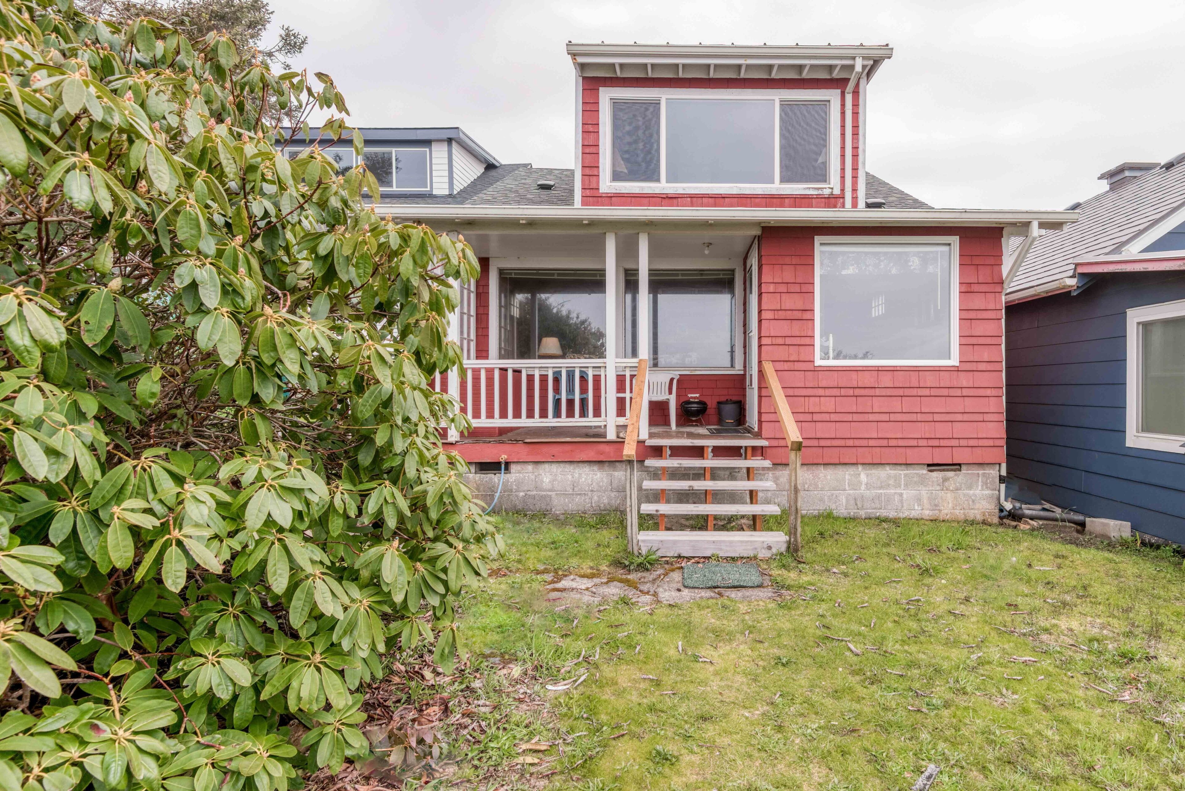 A two-story house with a red exterior, a front porch, and a small front yard.