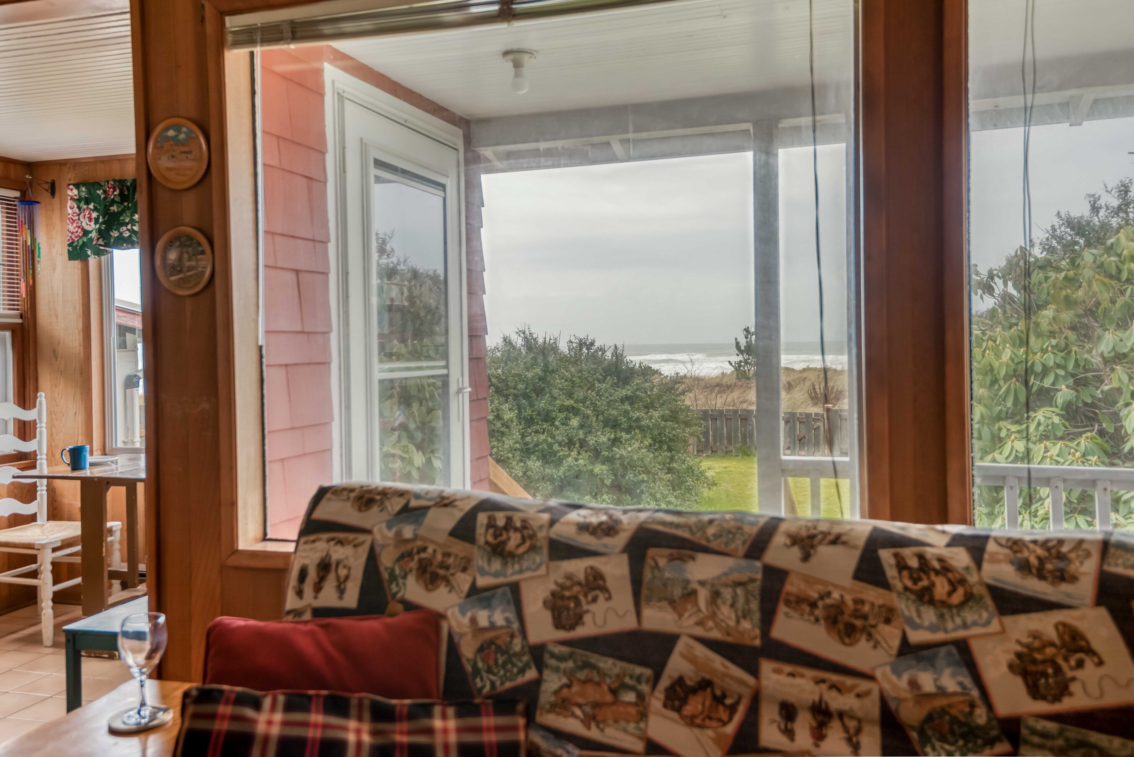 A cozy room with a large window, a wooden table with chairs, and a patterned sofa.