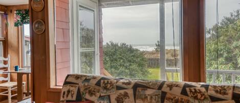 A cozy room with a large window, a wooden table with chairs, and a patterned sofa.