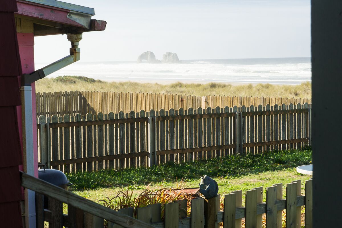 A wooden fence, a bird on a post, and a view of the ocean with distant rock formations.