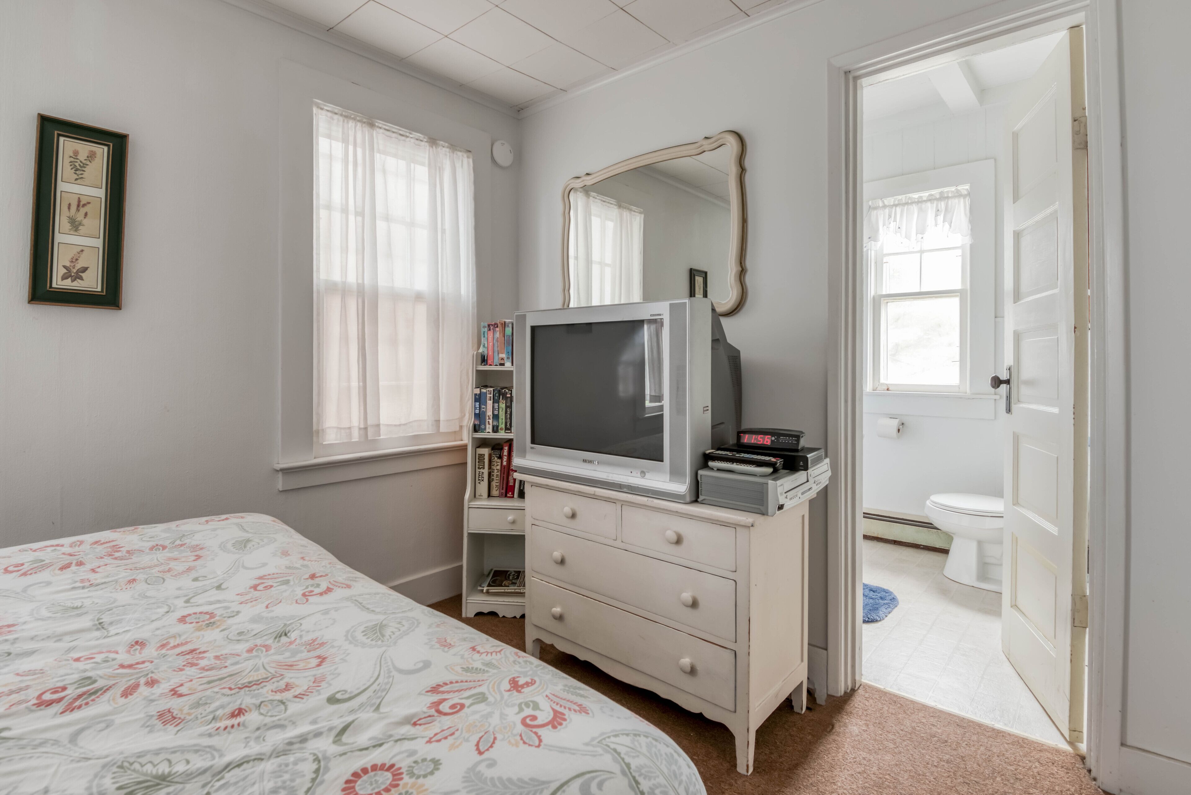 A bedroom with a bed, dresser, television, and a door leading to a bathroom.