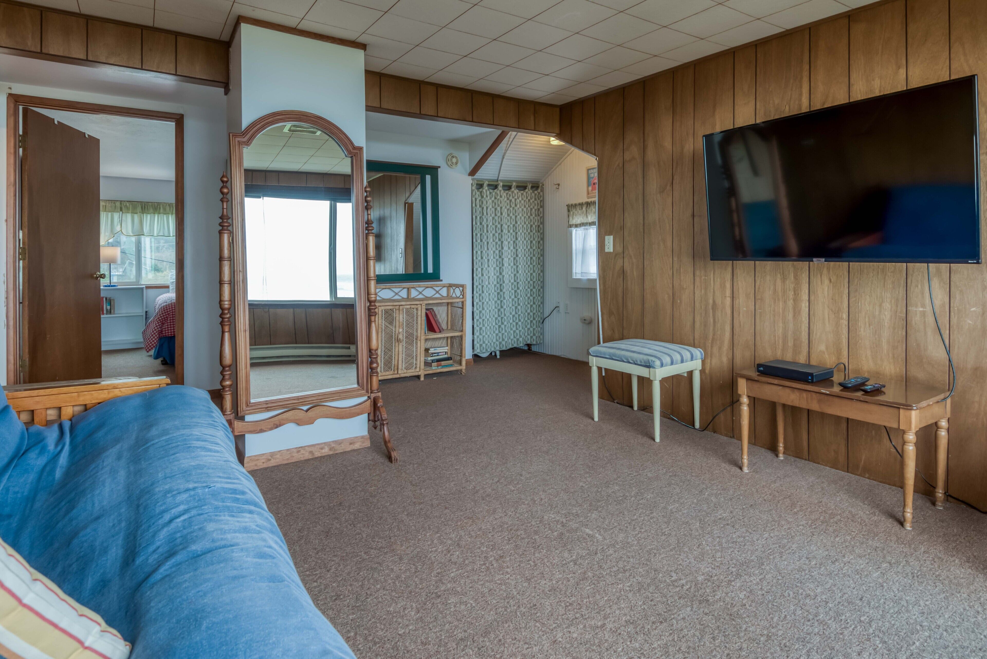 A room with a bed, a wooden bench, a dresser, a mirror, and a television.