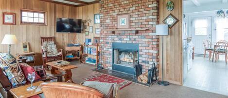 A cozy living room with a brick fireplace, wooden beams, a television, and comfortable seating.