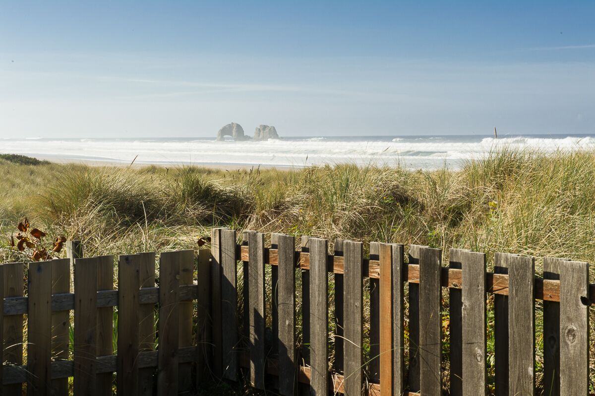 Ein Holzzaun im Vordergrund, im Hintergrund ein Strand und das Meer.