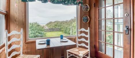 A wooden interior with a dining table and chairs, a window with a view of greenery, and a door with decorative plates.