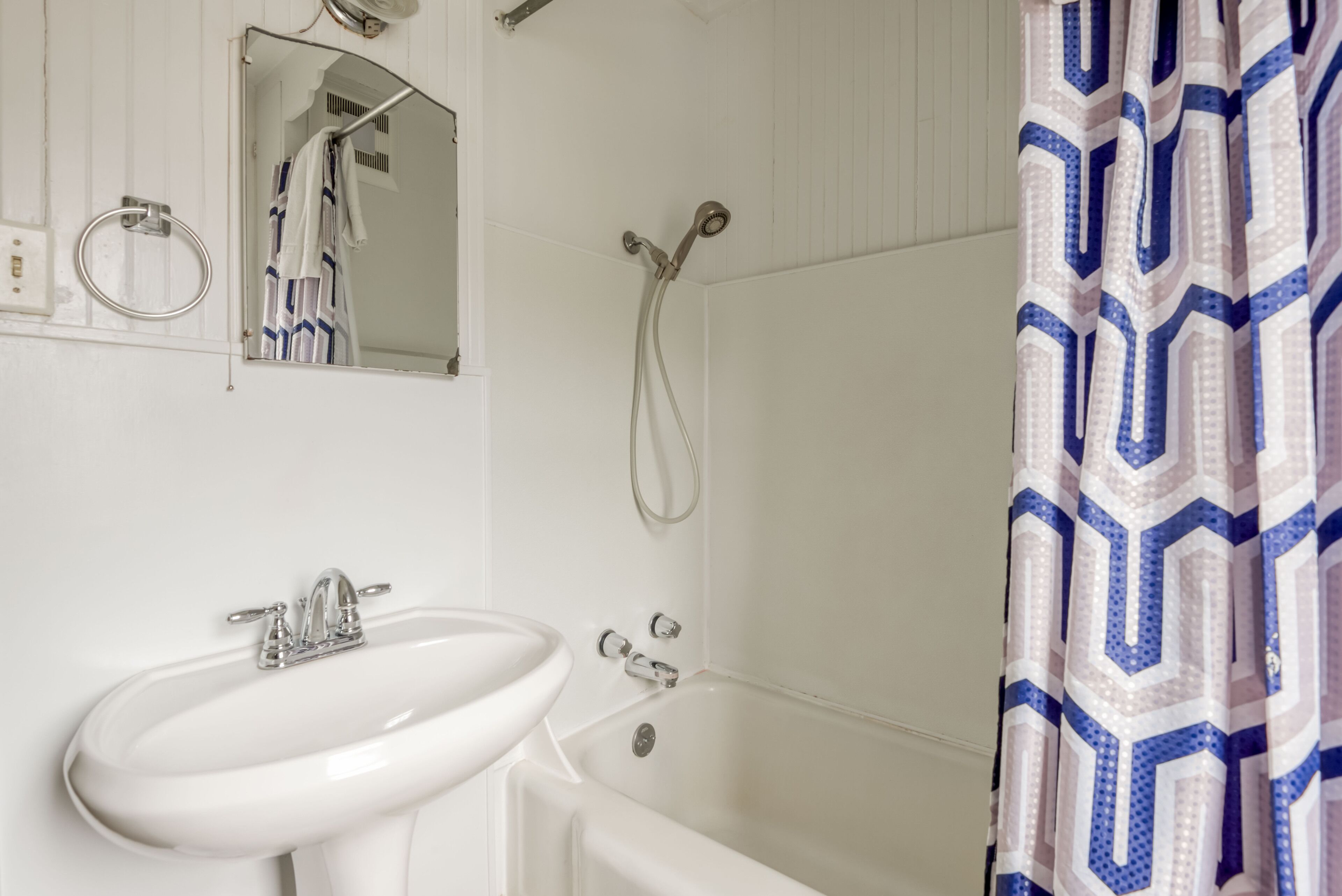 Un baño con un lavamanos blanco, un espejo, una ducha y una cortina de ducha estampada.