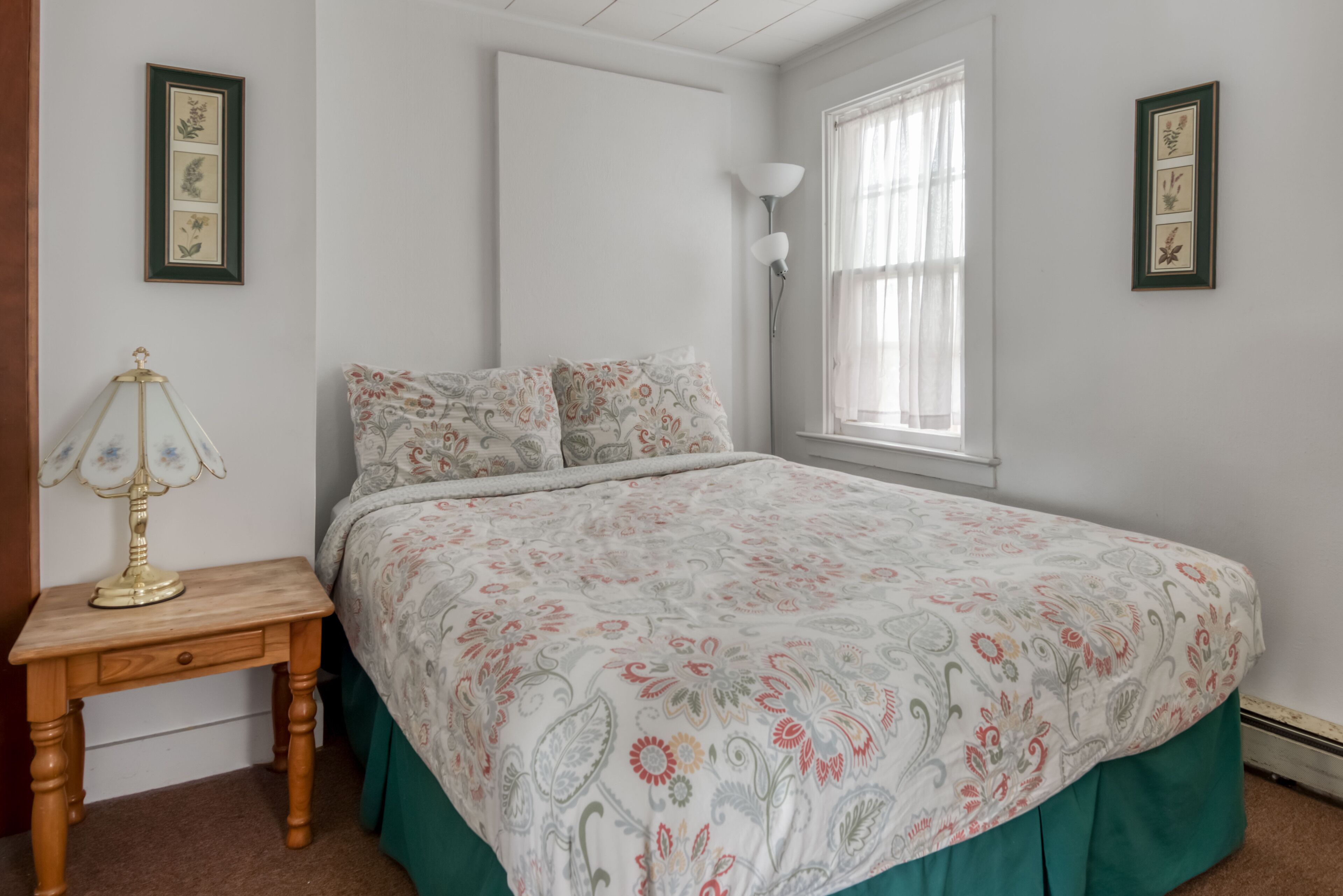 Un dormitorio con una cama, una mesita de noche, una lámpara y cuadros en las paredes.