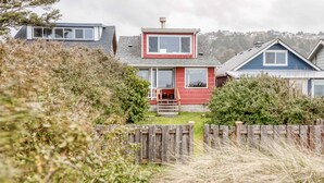 Ein modernes Haus mit roter Fassade, großen Fenstern und einer sichtbaren Veranda.