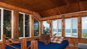 Een houten chalet met een bed, grote ramen en uitzicht op de oceaan.