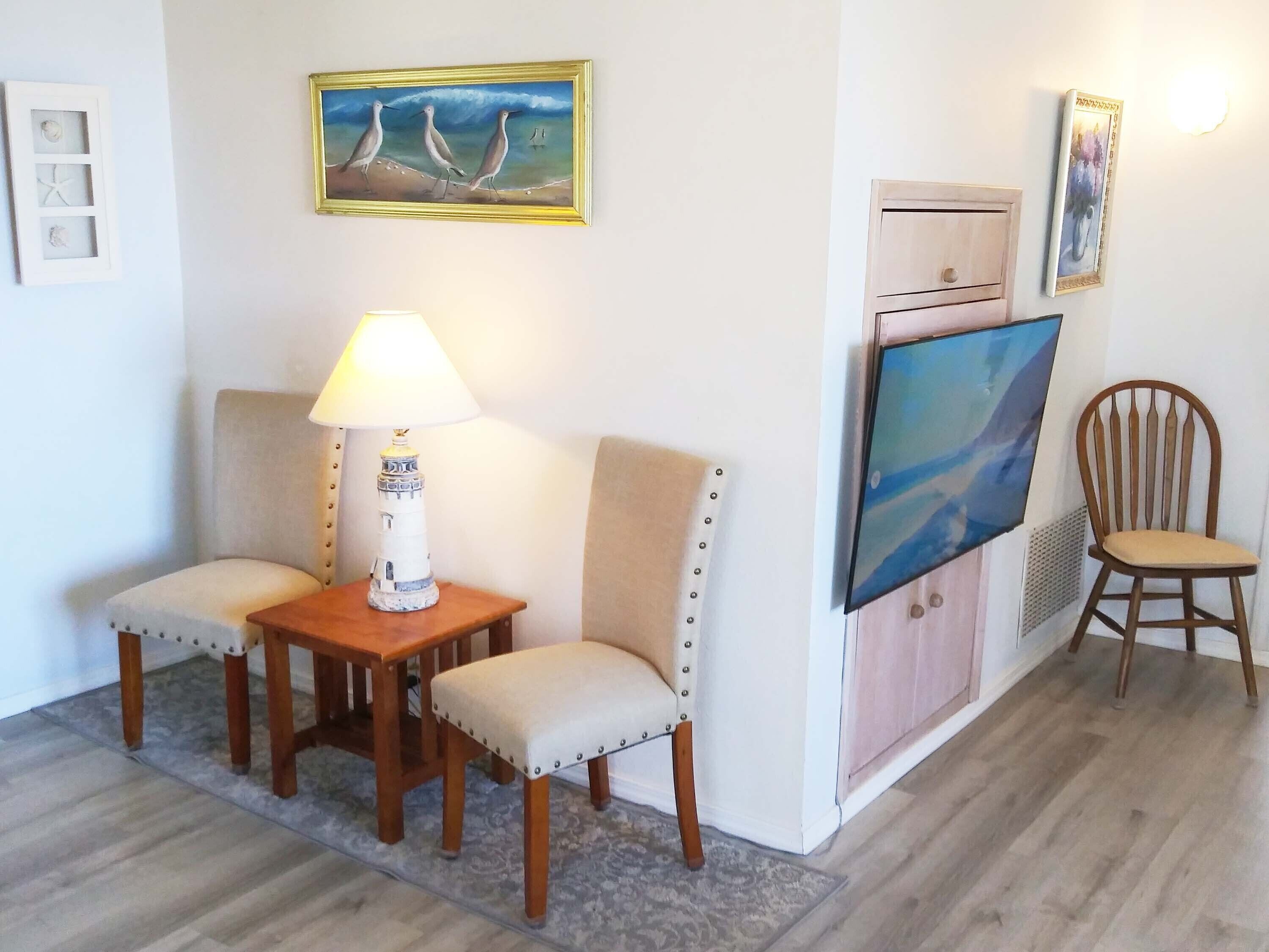 A living room with a sofa, two armchairs, a small table with a lamp, a television, and a chair.