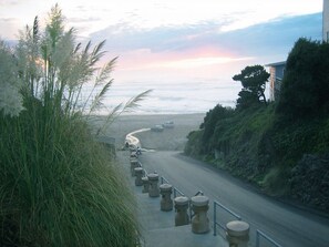Eine Küstenstraße mit Gehweg, Geländer und einem Strand im Hintergrund.