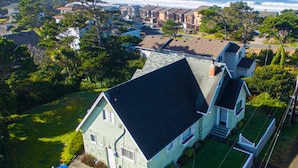 A two-story house with a dark roof, surrounded by lush greenery and a view of the ocean. - Spacious home, easy beach access, central location close to local attractions (Lincoln City)