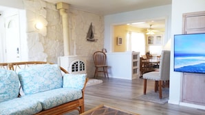 A living room with a stone wall, a white heater, a wicker sofa, a glass coffee table, and a dining area with chairs and a table. - Spacious home, easy beach access, central location close to local attractions (Lincoln City)