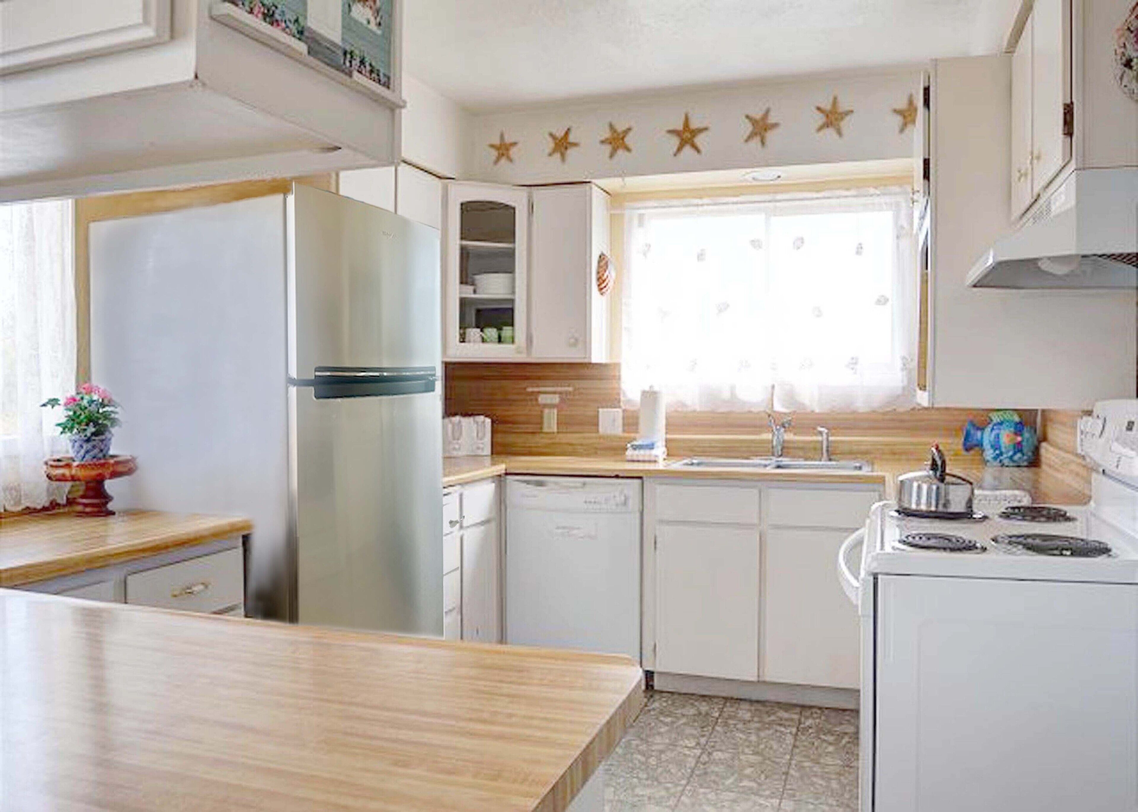 A compact kitchen with white cabinets, a built-in dishwasher, a refrigerator, and a window with star decorations above it.
