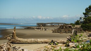 A beach with driftwood, a wooden pier, and a building with a lighthouse-like structure.
