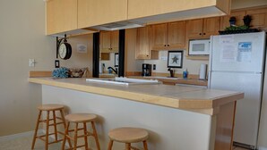 A kitchen with wooden cabinets, a microwave, a refrigerator, and three wooden stools.