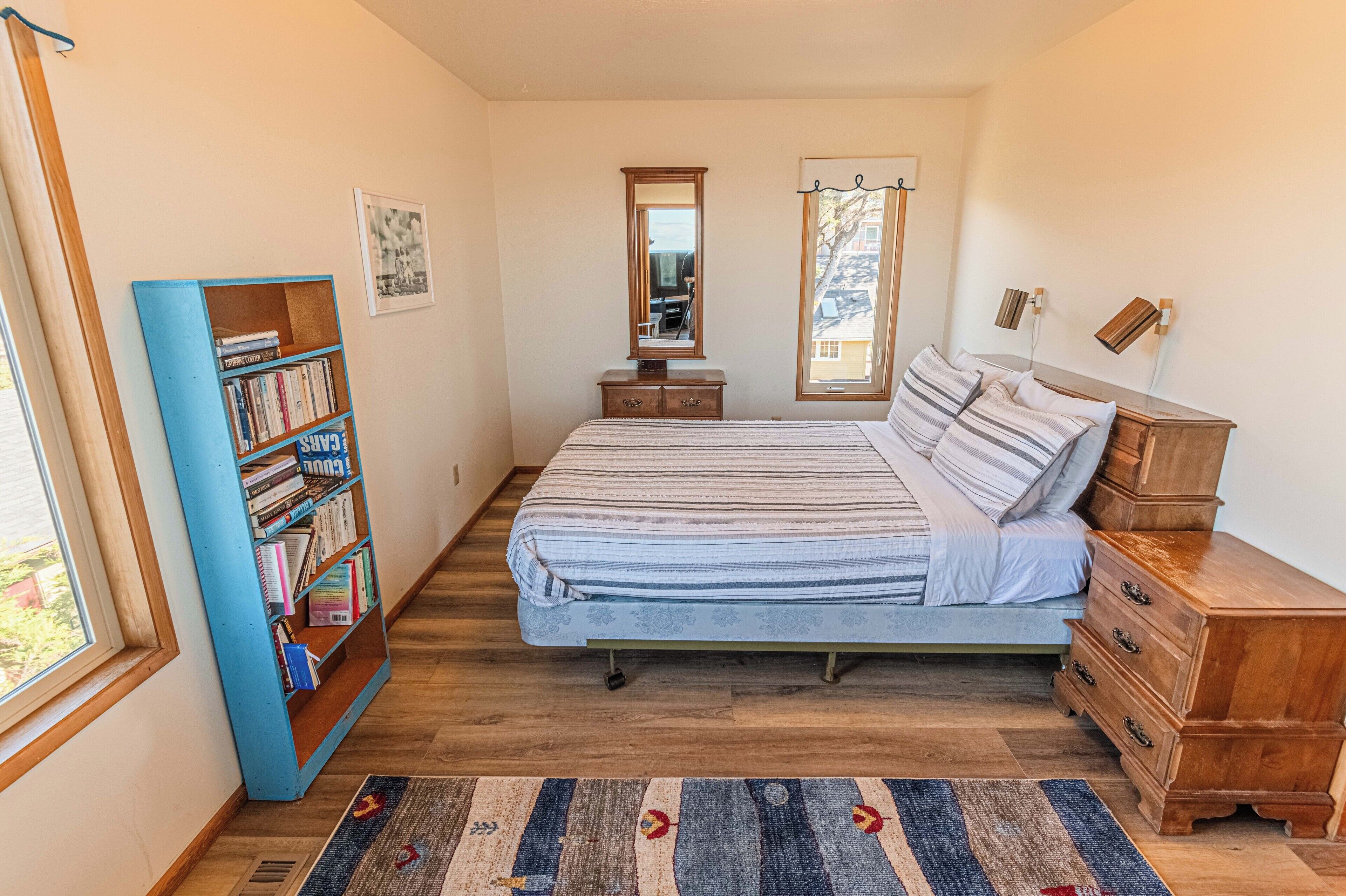 Une chambre à coucher avec un lit, une commode en bois, une bibliothèque, un miroir et une fenêtre.