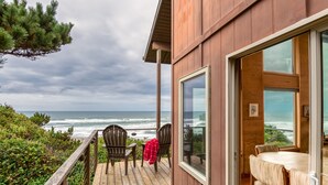 A wooden deck with a view of the ocean, two chairs, and a table with a red blanket. - Oceanfront Home, Deck, High Windows with Amazing Views, Beach Access Nearby (Lincoln City)