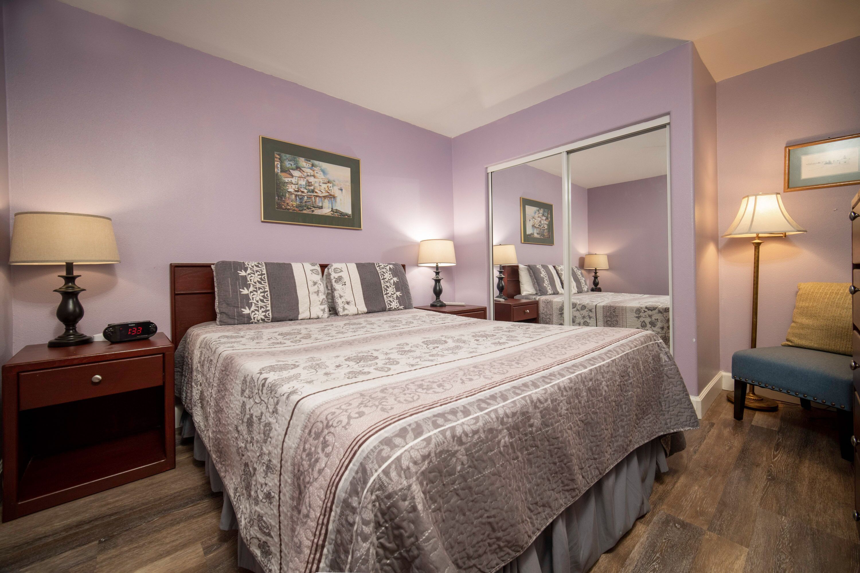 A bedroom with a large bed, two bedside tables with lamps, a chair, and a mirror.