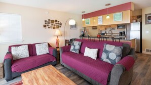 Un salon confortable avec un canapé et une table basse, une cuisine dotée de meubles en bois et d’un réfrigérateur, et un coin repas avec une table et des chaises.