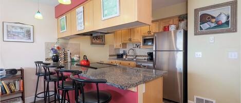 A kitchen with a central island, bar stools, a stainless steel refrigerator, and a microwave.
