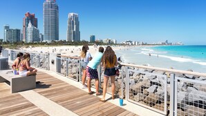 A beachside promenade with a view of the ocean and city skyline. - Private Condos at 101 Ocean by LMC (Miami Beach)