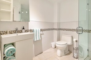 A modern bathroom with a white sink, a toilet, and a glass shower enclosure. - Private Condos at 556 Ocean by LMC (Miami Beach)