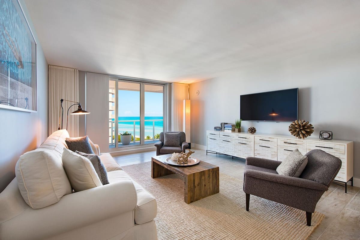 A modern living room with a sofa, armchair, coffee table, and a TV on a white cabinet.