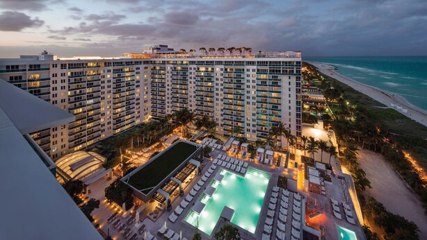 A high-rise hotel with multiple balconies overlooking a beach and a pool area with sun loungers. - 1 Homes Vacation Rentals by LMC (Miami Beach)