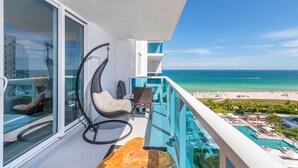 A balcony with a view of the ocean, a lounge chair, a dining table, and a pool area. - 1 Homes Vacation Rentals by LMC (Miami Beach)