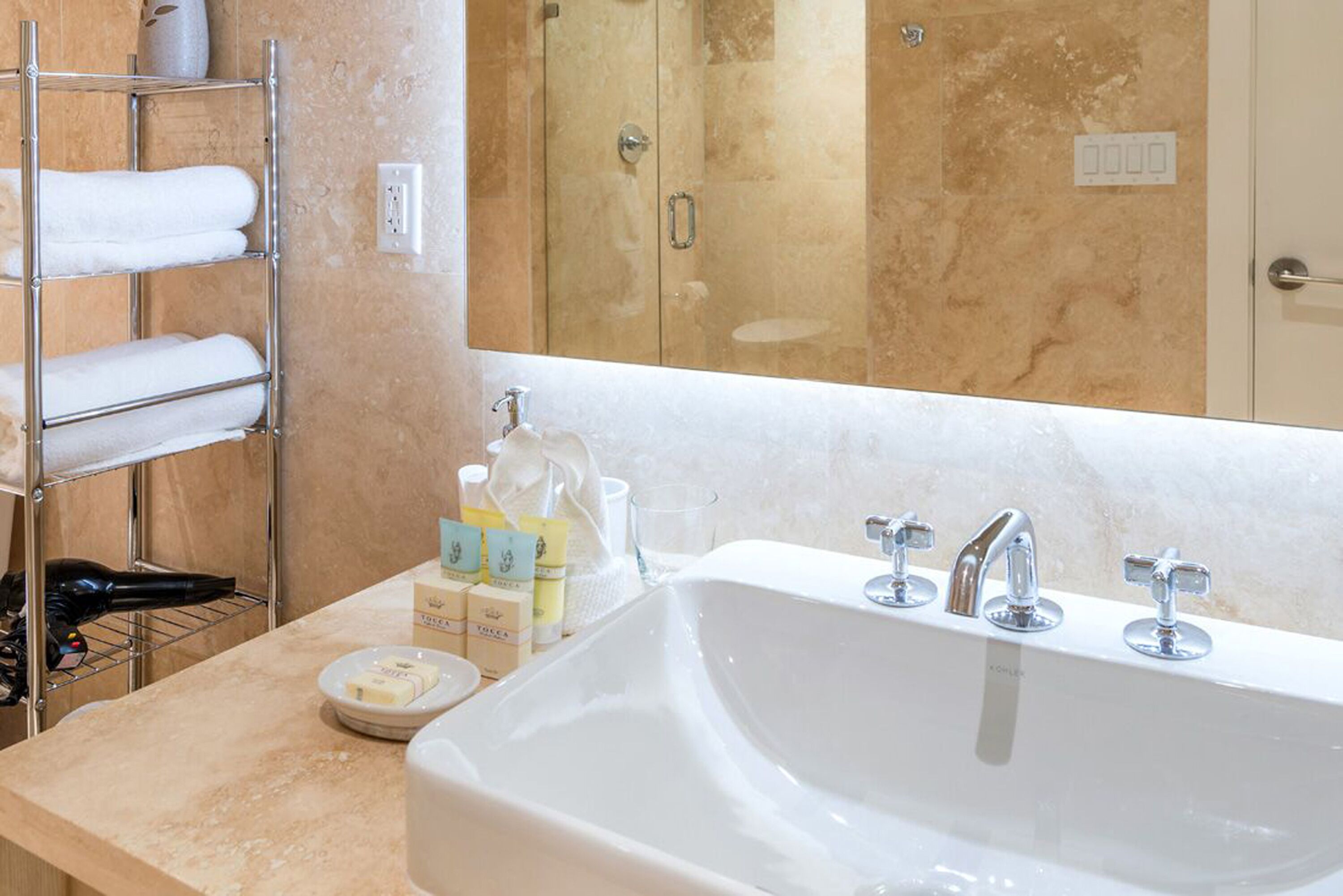 A bathroom with a large sink, a towel rack with folded towels, and toiletries on the counter.
