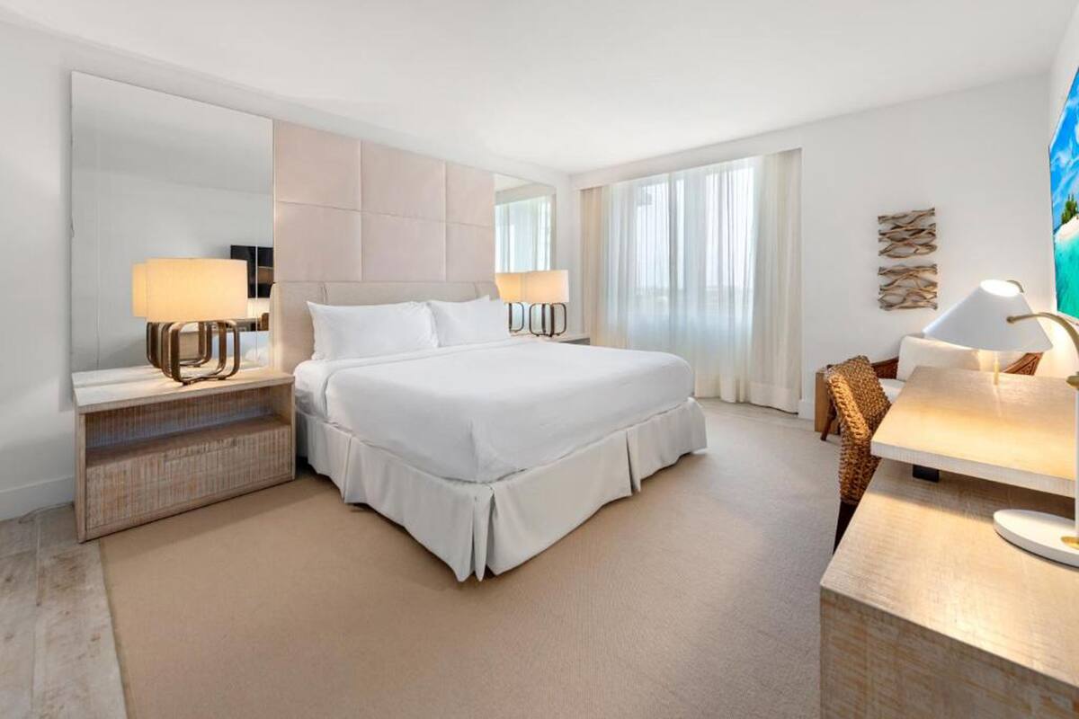 A hotel room with a large bed, bedside lamps, a desk, and a large mirror.