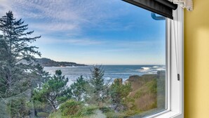 A coastal view from a window overlooking the ocean, trees, and a distant hill.