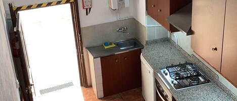 A compact kitchen with a gas stove, sink, and wooden cabinets.