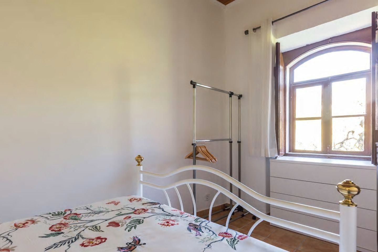 A bedroom with a bed, a window with curtains, and a metal wardrobe.