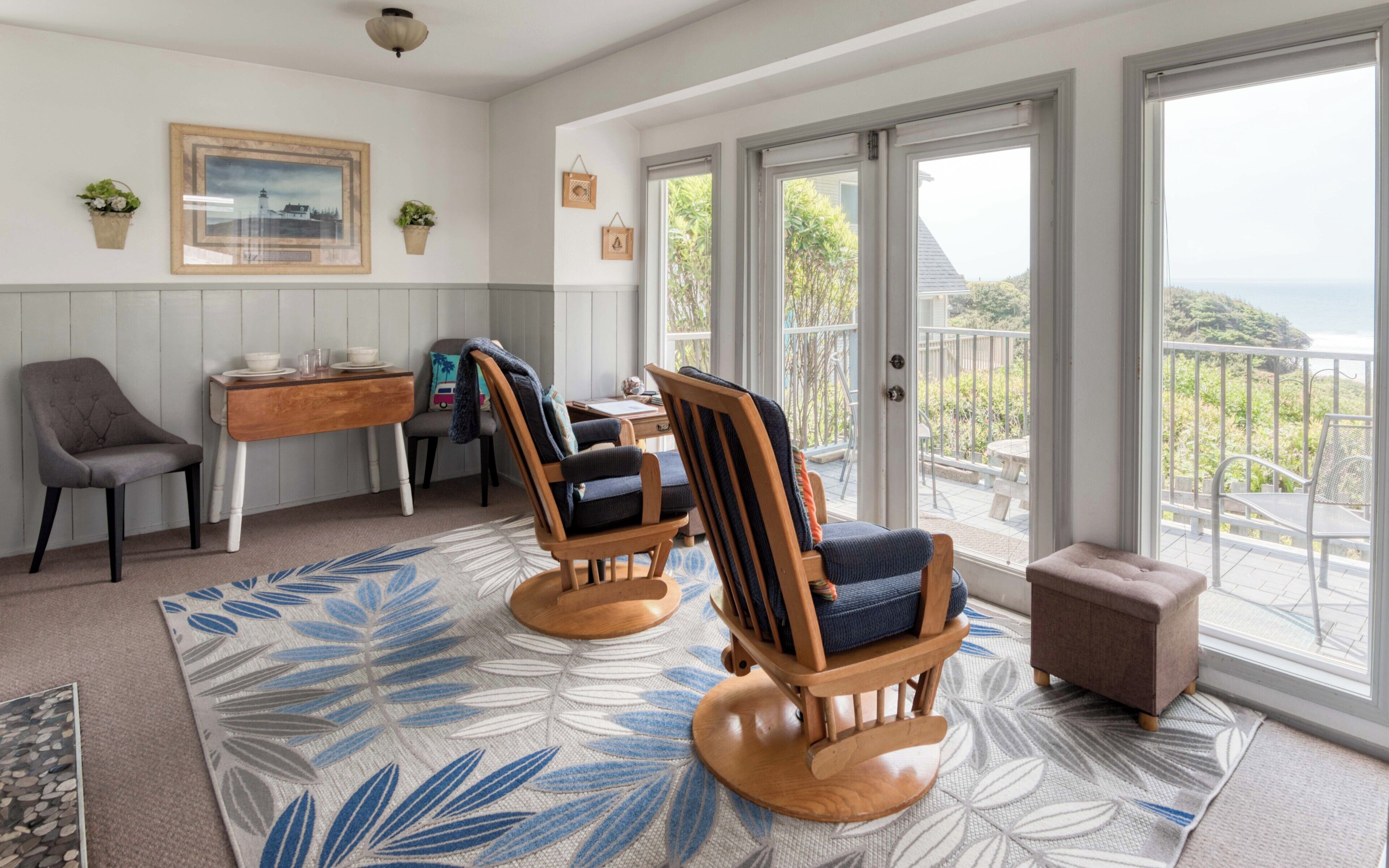 A cozy room with a wooden desk, two rocking chairs, a small table, and a view of the outdoors.