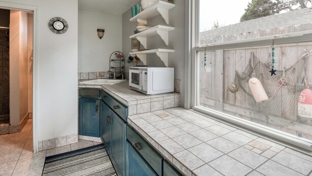 A kitchen with white cabinets, a microwave, and a window with a view of a wooden fence and trees.