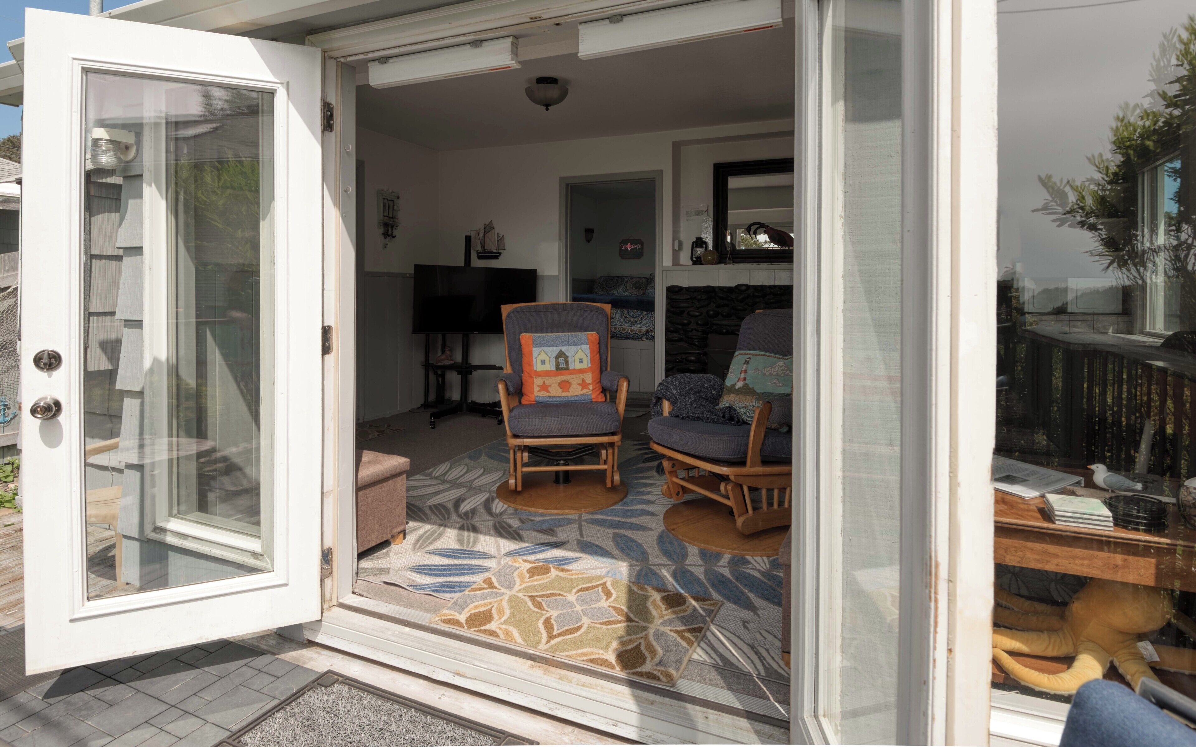 An open sliding glass door leading to a living area with two rocking chairs, a television, and a patterned rug.
