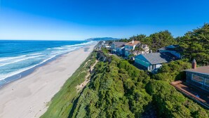A coastal property with beachfront houses, a sandy beach, and dense greenery. - Take in panoramic views from the living room or deck at this oceanfront home (Lincoln City)