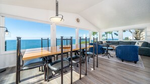A dining area with a wooden table and chairs, a sofa, and a view of the ocean. - Take in panoramic views from the living room or deck at this oceanfront home (Lincoln City)