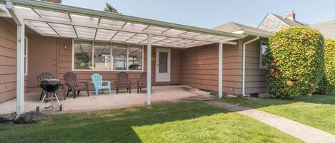 A covered patio with a grill, outdoor seating, and a well-maintained lawn.