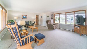 Ein gemütliches Wohnzimmer mit einer Couch, zwei Sesseln, einem Couchtisch und einem Fernseher auf einem Holzboden.